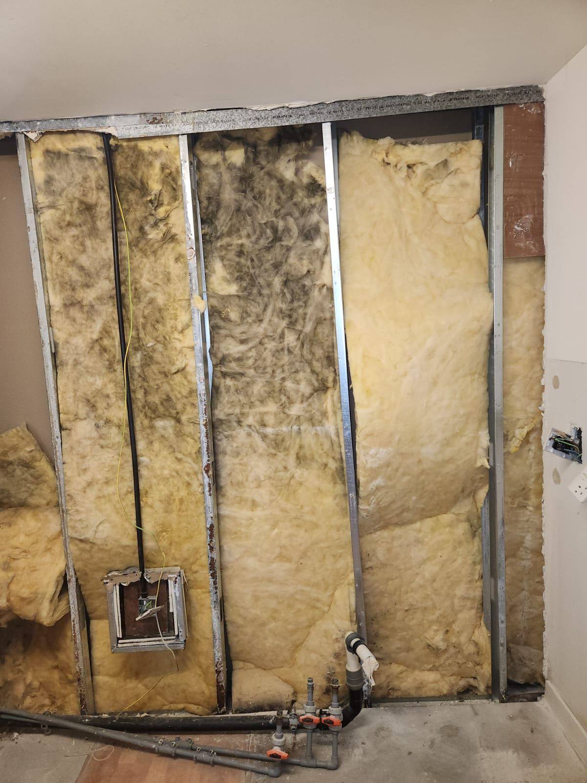 Contaminated mineral wool insulation exposed within the metal studwork